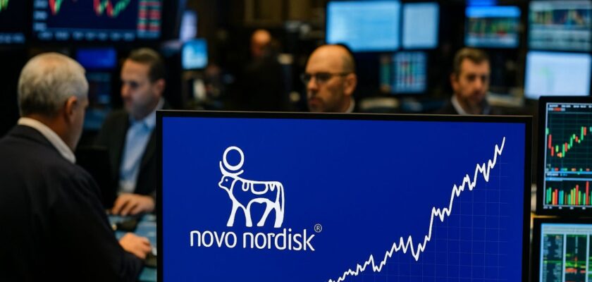 Una sala della Borsa con degli schermi con grafici finanziari. Il logo Novo Nordisk sullo schermo in primo piano