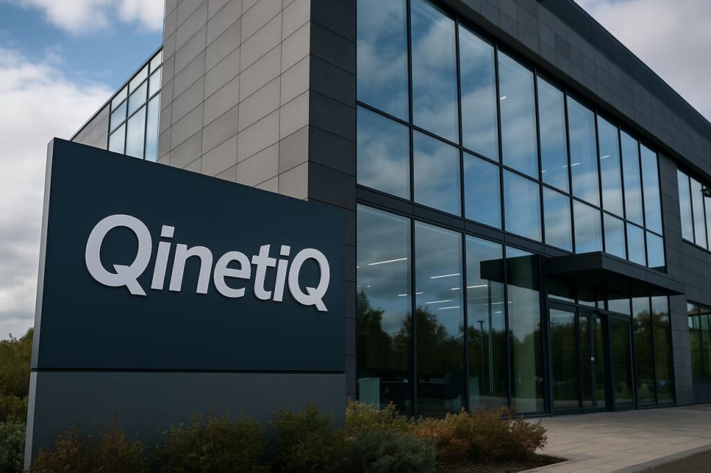Un totem pubblicitario con la scritta QinetiQ e un edificio con una grande vetrata sullo sfondo