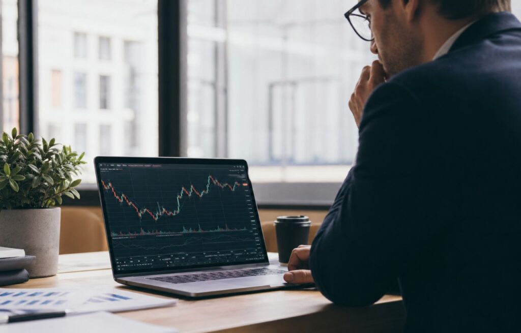 Professionista al desk osserva grafici finanziari sul laptop in un ufficio