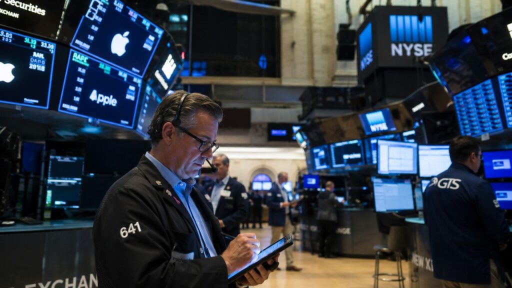 Trader al NYSE circondato da monitor finanziari e dati di mercato in tempo reale