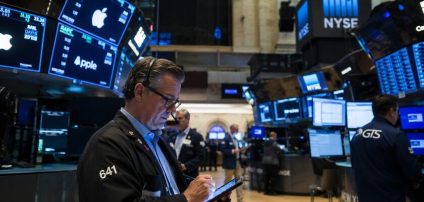 Trader al NYSE circondato da monitor finanziari e dati di mercato in tempo reale