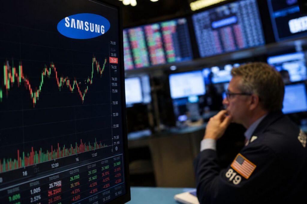 Sala produttiva di semiconduttori Samsung con trader screen finanziari sullo sfondo