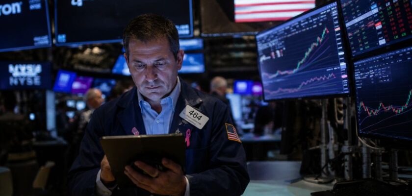 Trader nella sala della Borsa di New York davanti a monitor finanziari con grafici azionari e logo Micron sullo sfondo