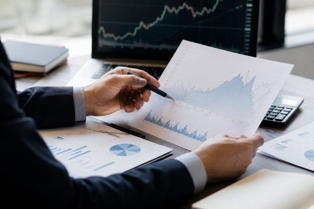 Professionista analizza grafici finanziari e dati di mercato su documenti e computer in un ufficio moderno