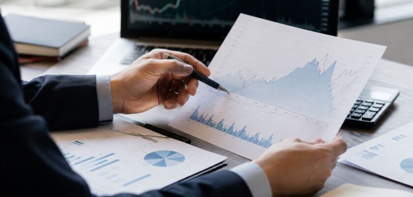 Professionista analizza grafici finanziari e dati di mercato su documenti e computer in un ufficio moderno