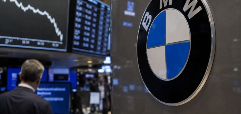 Logo BMW in primo piano davanti a monitor finanziari con grafici in calo, all'interno di una sala operativa di Borsa
