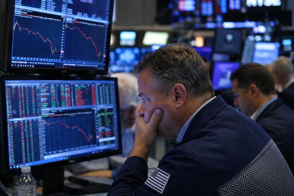 Trader preoccupato davanti a schermi finanziari con grafici in forte ribasso all'interno di una sala operativa di borsa