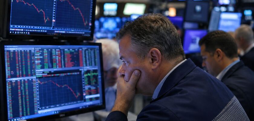Trader preoccupato davanti a schermi finanziari con grafici in forte ribasso all'interno di una sala operativa di borsa