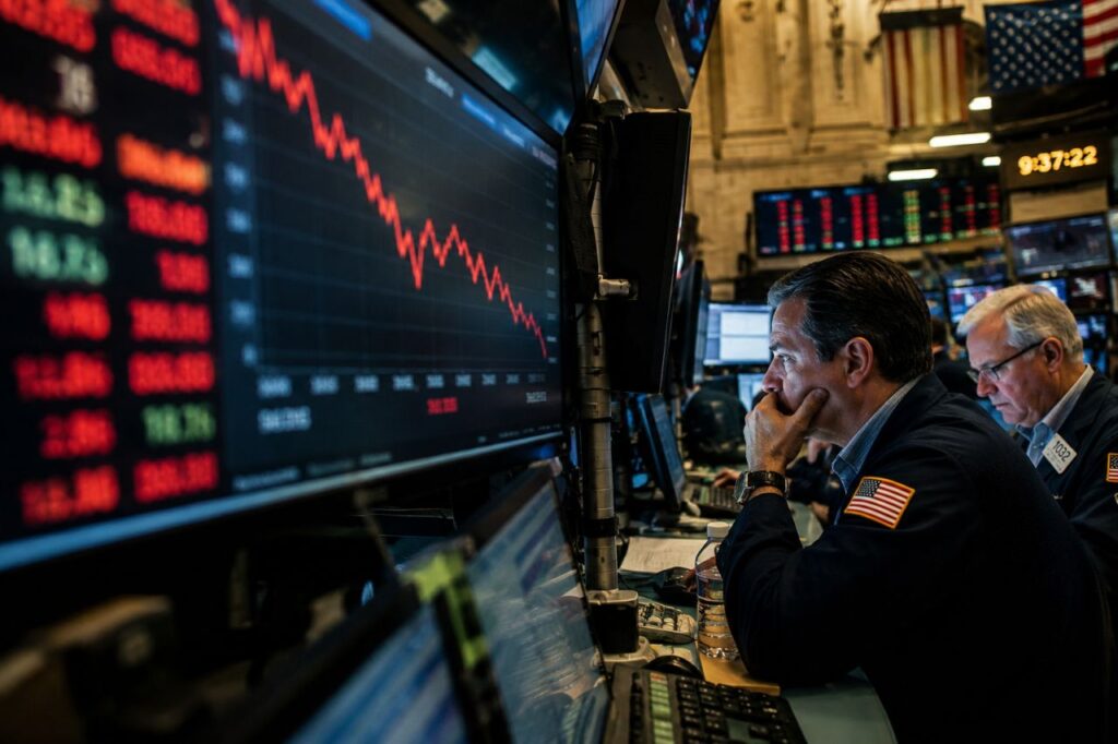 Trader osservano schermi finanziari con grafici in forte ribasso all'interno di una sala operativa di Borsa.