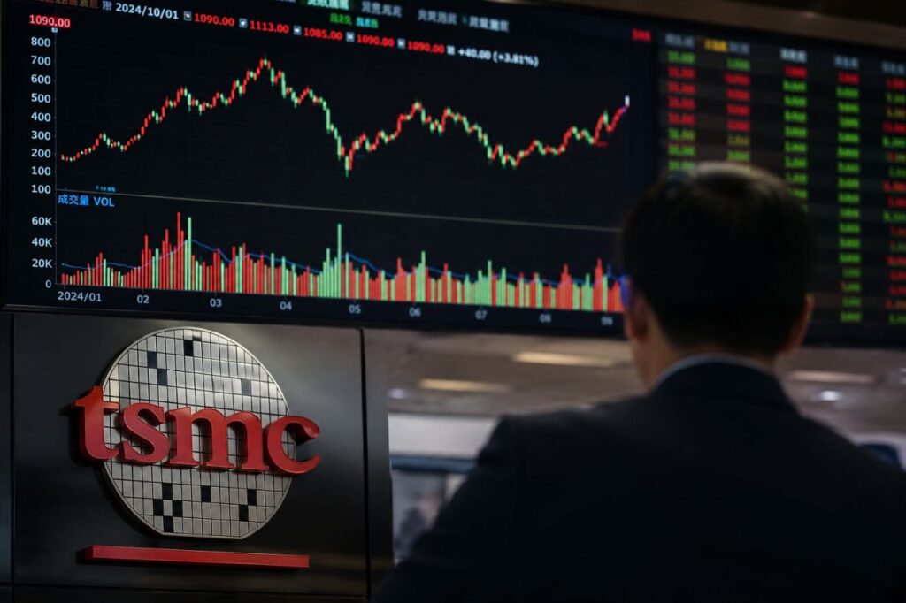 Uomo in giacca osserva un grande monitor con grafici di Borsa; in primo piano è visibile il logo TSMC, richiamo al settore dei semiconduttori e degli investimenti finanziari