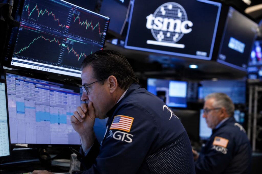 Trader davanti a monitor con grafici di Borsa e logo TSMC, in una sala operativa finanziaria