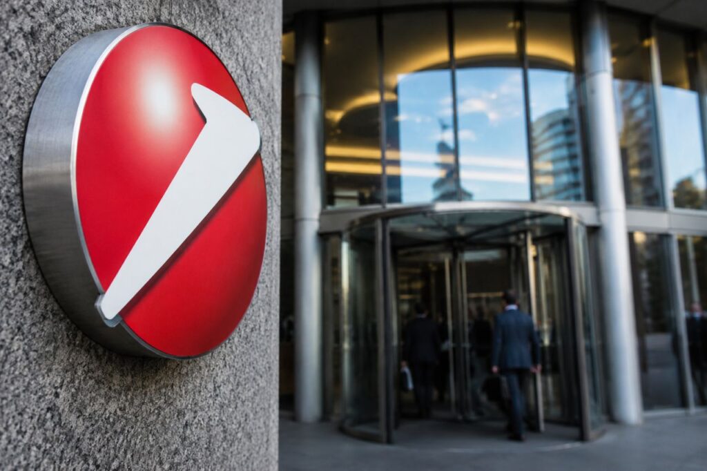 Ingresso di una moderna sede bancaria con il logo UniCredit in primo piano e professionisti che entrano nell'edificio