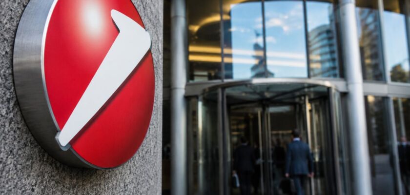 Ingresso di una moderna sede bancaria con il logo UniCredit in primo piano e professionisti che entrano nell'edificio