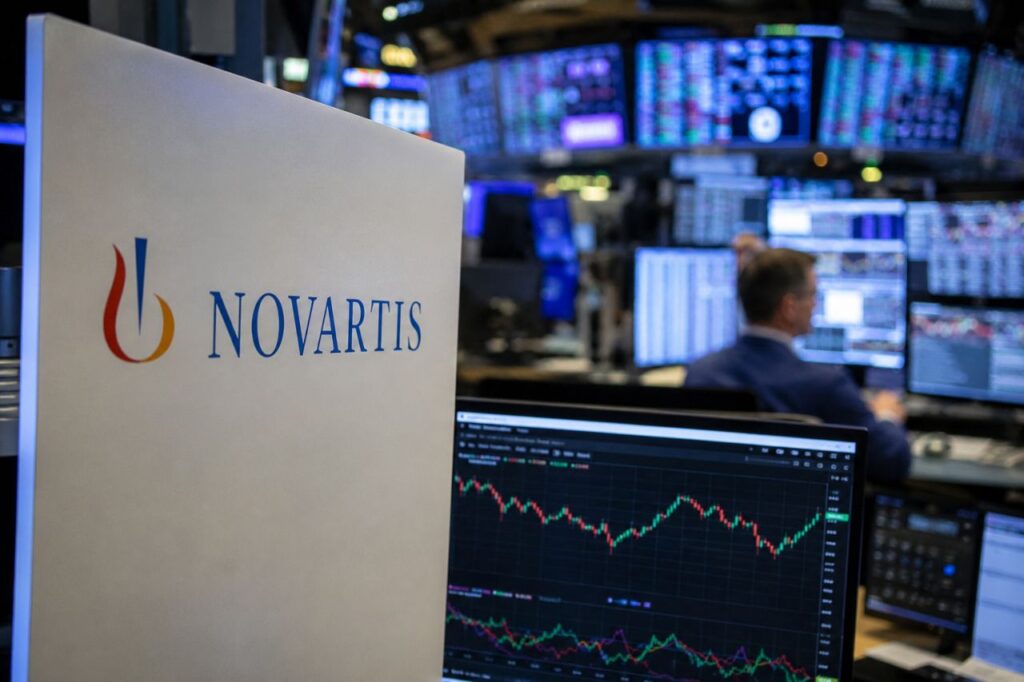 Logo Novartis accanto a monitor con grafici di Borsa in una moderna sala operativa finanziaria