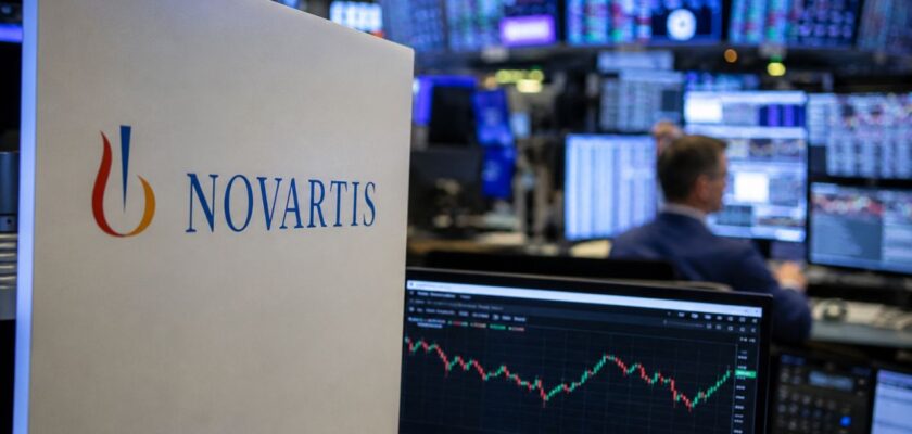 Logo Novartis accanto a monitor con grafici di Borsa in una moderna sala operativa finanziaria