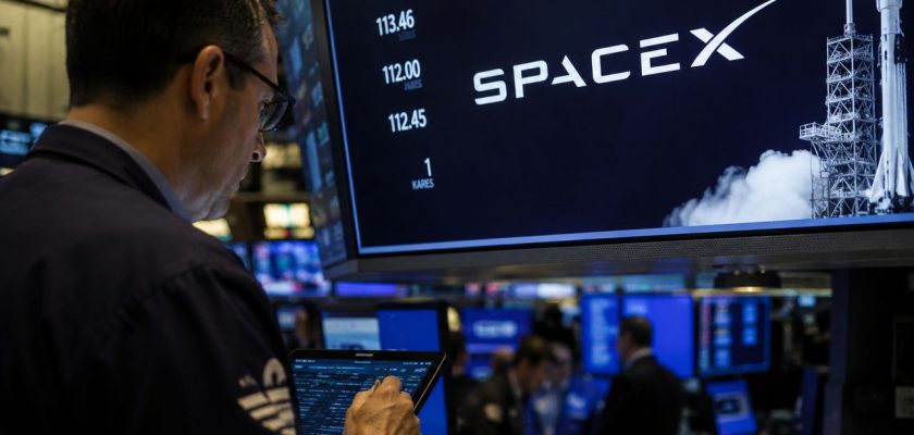 Operatore finanziario davanti a monitor con il logo SpaceX e un razzo, in una sala di trading