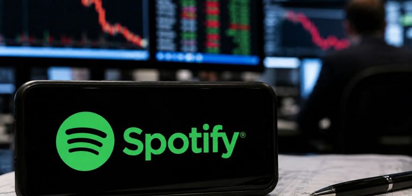 Smartphone con logo Spotify su documenti finanziari, davanti a monitor di Borsa con grafici in calo