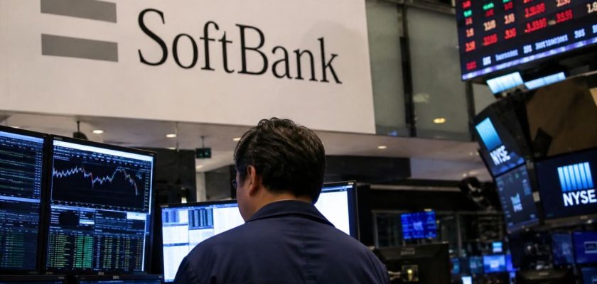 Operatore finanziario davanti a monitor di borsa in una sala di trading, con logo SoftBank e schermate di mercato sullo sfondo