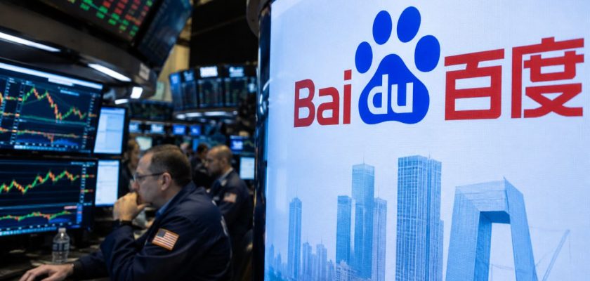 Sala trading con operatori e monitor finanziari, accanto a un grande schermo con il logo Baidu