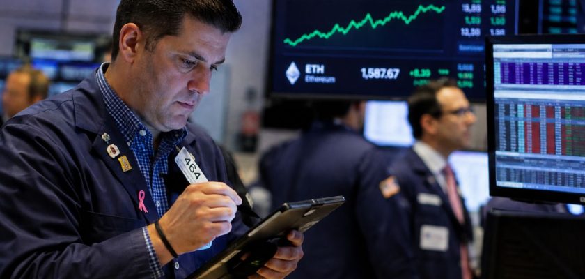 Trader al lavoro su un tablet, circondato da monitor finanziari con grafici di mercato in rialzo