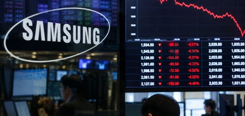 Logo Samsung accanto a monitor finanziari con grafico azionario in forte calo e operatori al lavoro