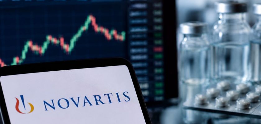 Logo Novartis in primo piano, grafico di Borsa sullo sfondo e flaconi di farmaci con compresse
