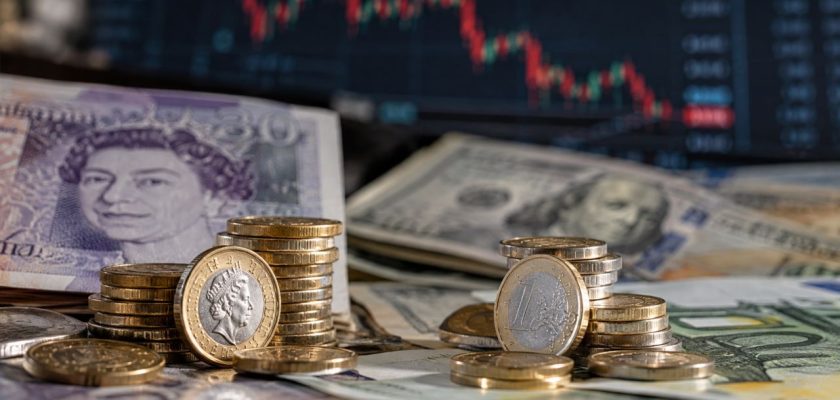 Banconote e monete in euro, sterline e dollari davanti a un monitor con grafico finanziario in calo