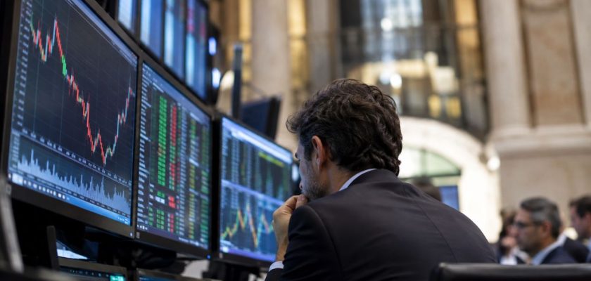 Operatore finanziario osserva monitor con grafici e quotazioni di Borsa, all’interno di una sala trading