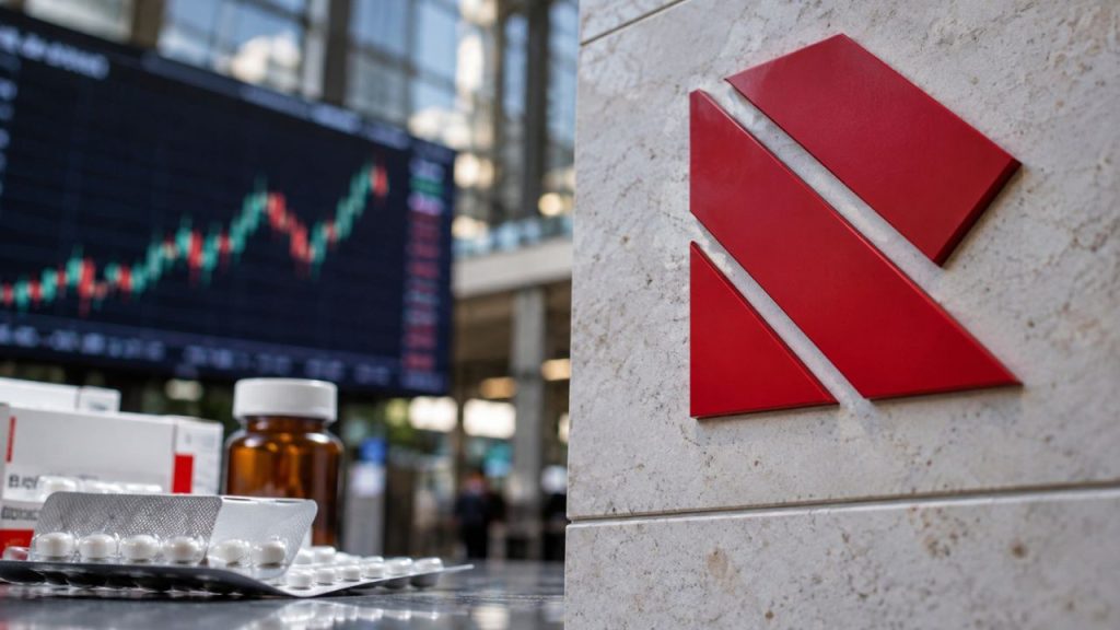 Logo rosso di Recordati su una parete in pietra, con confezioni di farmaci e blister di compresse in primo piano e un monitor con grafici di Borsa sullo sfondo