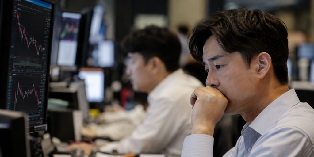 Due operatori finanziari asiatici osservano i grafici di Borsa sui monitor, in una sala trading